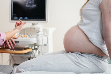 A pregnant girl is having an ultrasound of the abdomen in the clinic in close-up. Medical examination