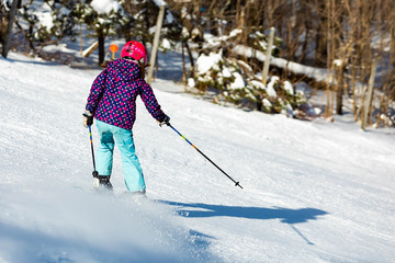 Skier girl performing slalom ride and having fun at resork in winter from the back