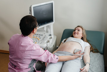 Obraz premium A pregnant girl gets an ultrasound of her abdomen at the clinic. Medical examination