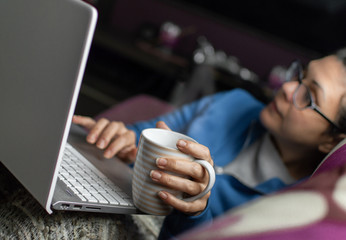 Woman sitting on a sofa with coffee cup using a laptop on a cold morning at home. Blur background.