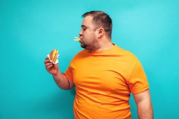 Emotional happy fat man on a blue background eating fast food hamburgers