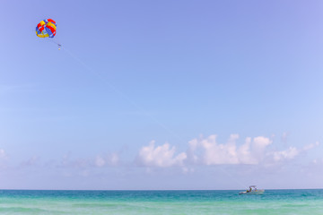 Bright parachute pulled by power boat on calm blue ocean - negative space and copy space