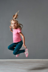 Fototapeta na wymiar Having fun. Portrait of a cute and excited little girl in casual clothes jumping in studio and looking at camera. Happy children. Childhood. Motion