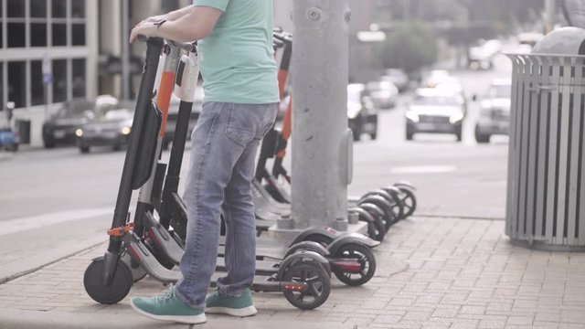 A man returns his scooter to a rental drop off on the sidewalk