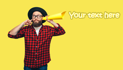 Handsome hipster guy secretly listening through yellow tube rolled up paper. Your text here! Discount, sale, season sales.