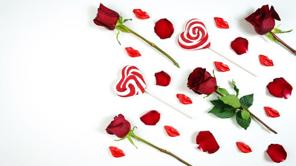 Red roses, petals, heart shaped lollipops and lip shaped chocolate kisses creative composition layout flat lay. Negative copy space.