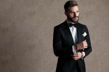 Confident groom fixing his sleeve and looking away