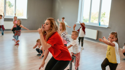 Keep silence. Portrait of a young female dance teacher holding index finger at lips while dancing with children in the dance studio. Choreography class