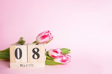 Obraz premium Pink tulips and march 8 wooden calendar on a pink background, space for text. Flat lay. 8 March, International Women's Day. 