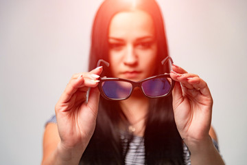 Woman holds and shows eyeglasses with black rim on a white background. Close-up
