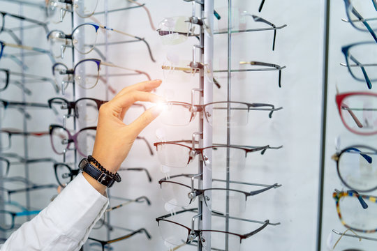 Row of glasses at an opticians. Eyeglasses shop. Stand with glasses in the store of optics. Woman's hand chooses spectacles. Eyesight correction. © Vadim