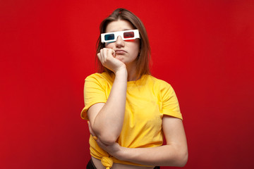 Fototapeta premium sad young girl watching a bad, boring movie in 3d glasses and with popcorn on a red background