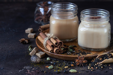 Two mason jars with Indian masala chai tea on dark stone background. Spiced hot tea with milk and...
