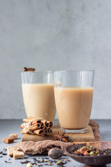 Two drinking glasses with traditional Indian drink - masala chai tea (milk tea) with spices on grey stone background with spices for making tea.
