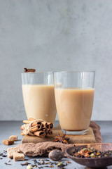 Two drinking glasses with traditional Indian drink - masala chai tea (milk tea) with spices on grey...