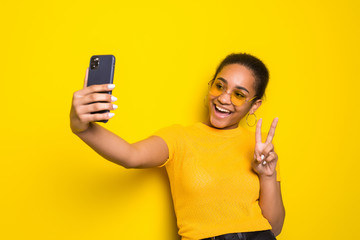 Young pretty latin woman selfie with peace gesture isolated yellow background