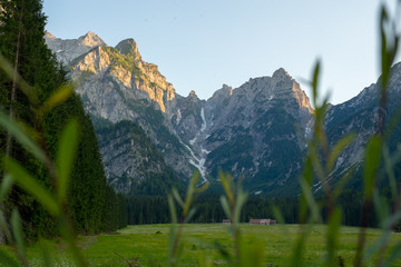 Green field and cottages under the alpine mountains on a sunny day in Julian Alps, Slovenia,...