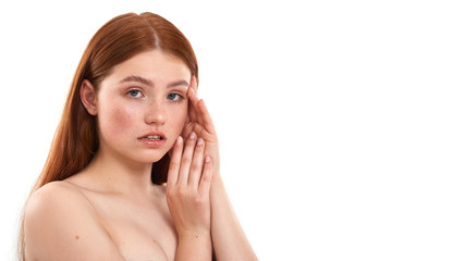 Fresh and clean. Portrait of a young sensual red-haired girl with freckles touching her face and looking at camera while standing against white background