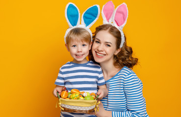 Happy easter! family mother and child son with ears hare getting ready for holiday on colored yellow background.