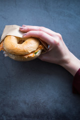 Woman's hand holding a salmon and rocket bagel. Vertical picture. Blogging concept.