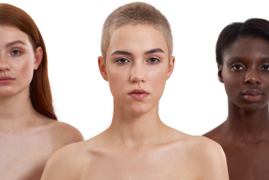 Three gorgeous multicultural young women looking at camera while posing in studio over white background.Beautiful models with black, red and blonde hair standing together
