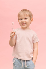 Happy child boy blond European appearance holding a toothbrush in his hands on a pink background.
