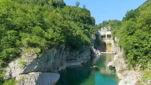 Drone flying low, over a narrow fresh water stream amidst green hills with hidden caves and waterfalls. Tourist destination.