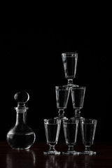 Obraz na płótnie Canvas Crystal decanter or carafe of vodka and glasses pyramid tower on wooden table in restaurant, black background for copy space