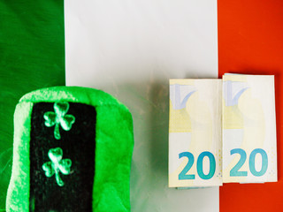 Green hat with shamrock two euro banknotes folded making 2020 year on Irish National flag, Saint Patrick day celebration. Dark background, copy space.