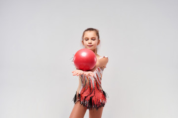 The power of balance. Flexible cute little girl child gymnast exercising using red ball isolated on a white background. Sport, training, rhythmic gymnastics, active lifestyle concept