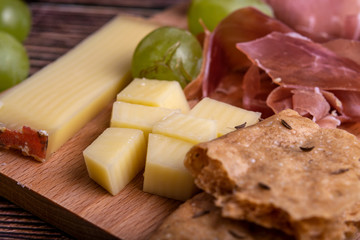 Close-up of a Bavarian snack, with ham, Swiss mountain cheese, crunchy rye bread and green grapes. Served on a wooden cutting board.