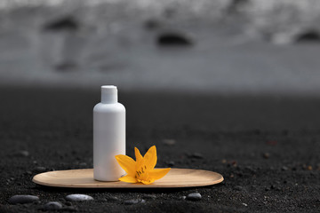 Empty white label cosmetics on black canarian beach. Skincare tube product on black sand with stones and ocean waves with white foam at the blurred background.