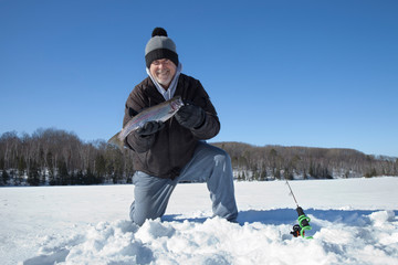 Fototapeta na wymiar Happy ice fisherman holds up freshly caught rainbow trout on a northern Minnesota lake