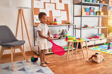 Beautiful african american toddler playing with tennis racket at kindergarten