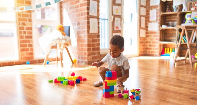 Beautiful african american toddler playing with wooden blocks train toy around lots of toys at kindergarten