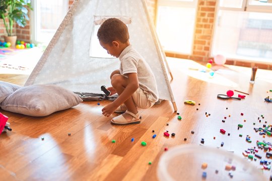 Beautiful african american toddler playing with cars around lots of toys at kindergarten