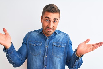 Young handsome man wearing denim jacket standing over isolated background clueless and confused...