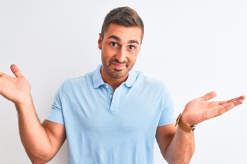 Fototapeta premium Young handsome elegant man wearing blue t-shirt over isolated background clueless and confused expression with arms and hands raised. Doubt concept.