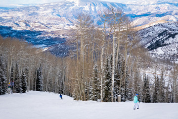 Scenic panoramic view as two skiers descend the slopes of the Aspen Snomass ski resort, in the Rocky Mountains of Colorado.  