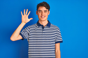 Fototapeta premium Teenager boy wearing casual t-shirt standing over blue isolated background showing and pointing up with fingers number five while smiling confident and happy.