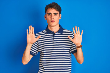 Teenager boy wearing casual t-shirt standing over blue isolated background Moving away hands palms showing refusal and denial with afraid and disgusting expression. Stop and forbidden.
