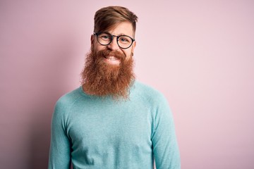 Handsome Irish redhead man with beard wearing glasses over pink isolated background with a happy...