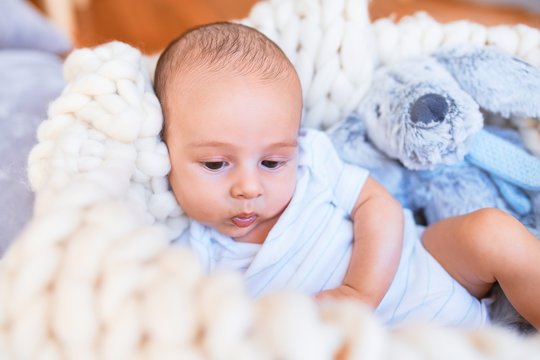 Adorable baby lying down over blanket on the floor at home. Newborn relaxing and resting comfortable with teddy bear