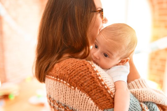 Young beautiful woman and her baby standing at home. Mother holding and hugging newborn