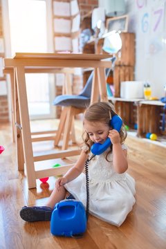 Adorable blonde toddler playing with vintage phone. Sitting on the floor around lots of toys at kindergarten