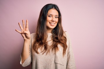 Young beautiful brunette woman wearing casual sweater standing over pink background showing and...