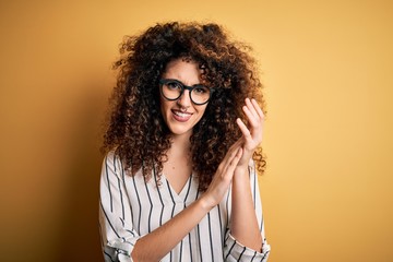 Young beautiful woman with curly hair and piercing wearing striped shirt and glasses clapping and applauding happy and joyful, smiling proud hands together