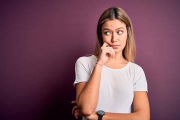 Fototapeta na wymiar Young beautiful blonde woman wearing casual white t-shirt over purple isolated background with hand on chin thinking about question, pensive expression. Smiling with thoughtful face. Doubt concept.