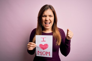 Fototapeta na wymiar Young beautiful woman holding paper with love mom message celebrating mothers day annoyed and frustrated shouting with anger, crazy and yelling with raised hand, anger concept