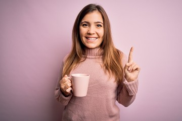 Young blonde woman drinking a cup of coffee over pink isolated background surprised with an idea or question pointing finger with happy face, number one